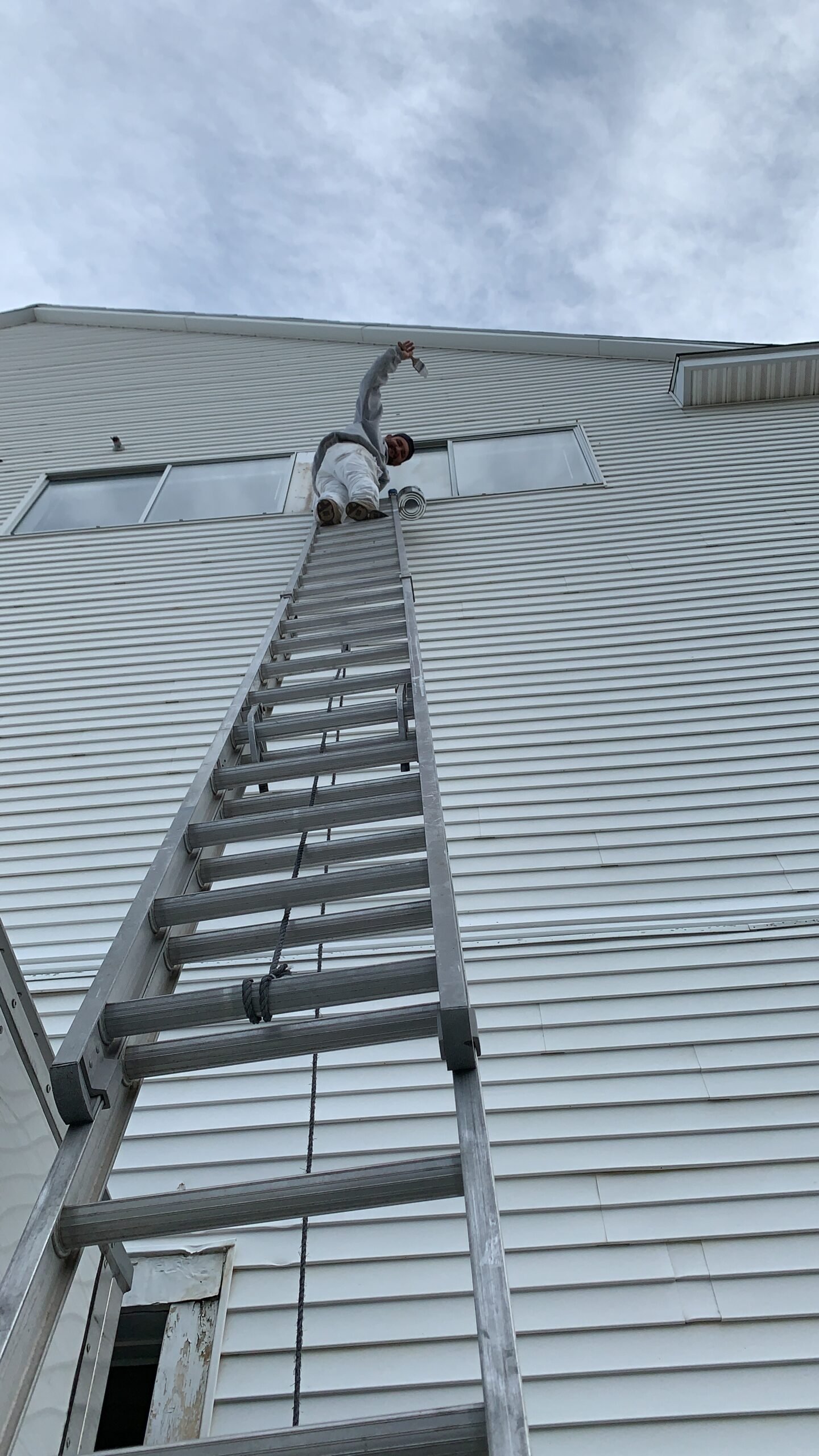 Fabricio Painting crew member on an extension ladder painting a Cape Cod home exterior